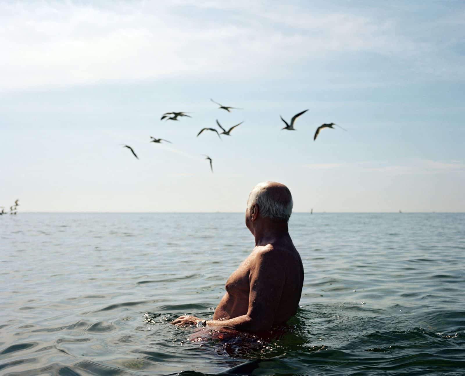 A man half-submerged in the ocean, with seagulls in the background