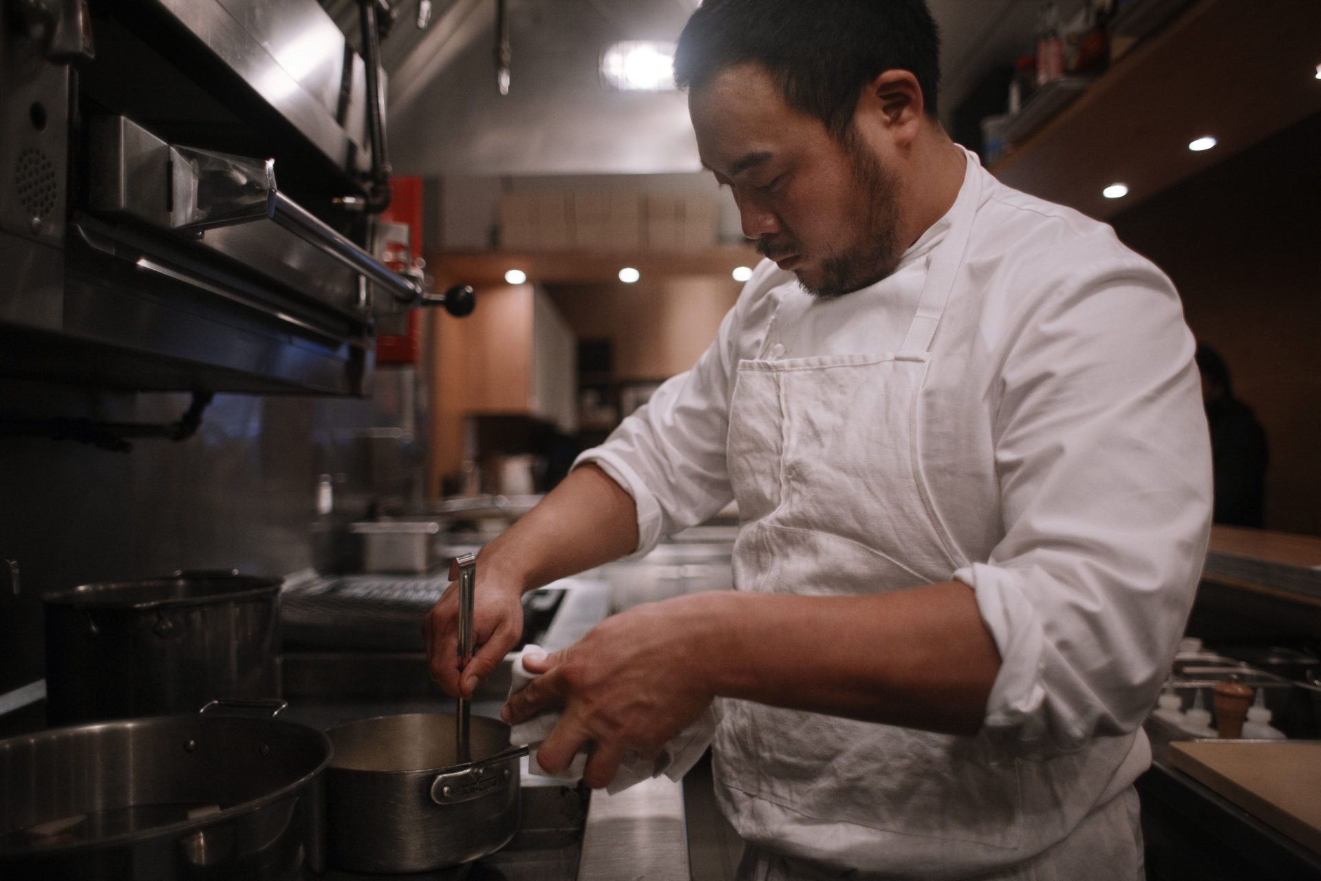 Chef David Chang stirring a pot in a restaurant kitchen. 