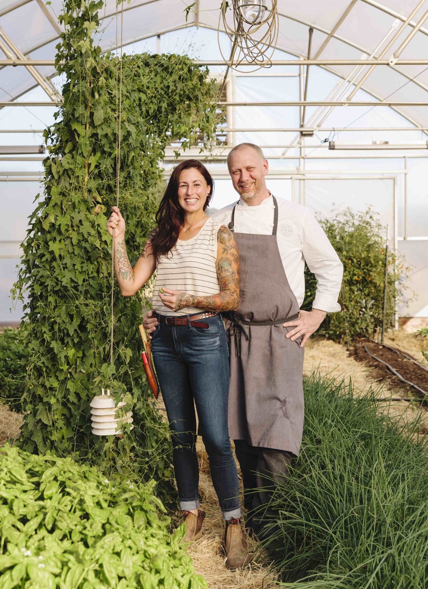 A woman and man standing in a greenhouse smiling at the camera. 