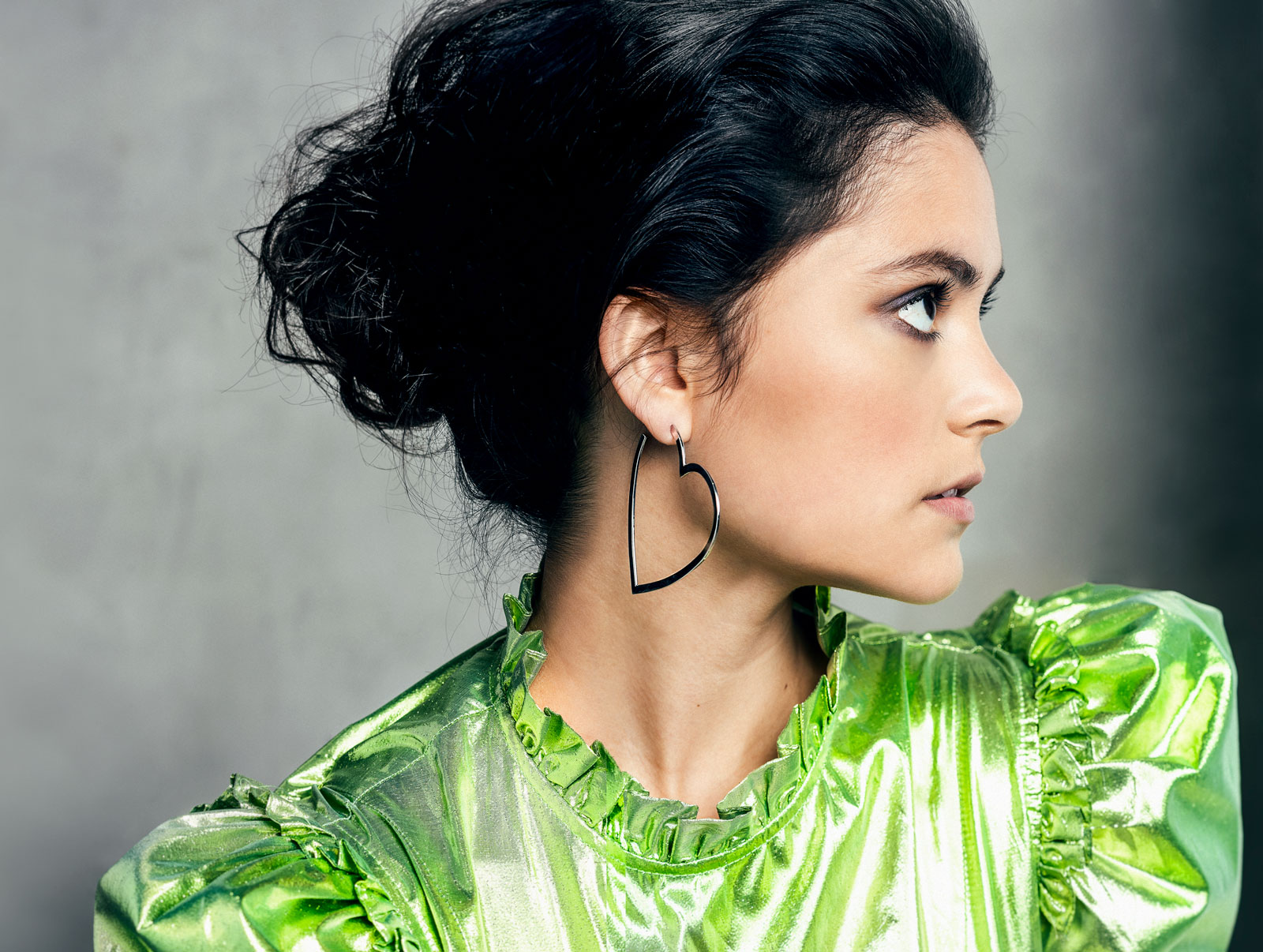 Actress Blu Hunt wearing a bright green shiny blouse, in profile.