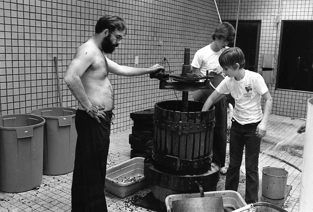A man and his two young sons using a wine press.