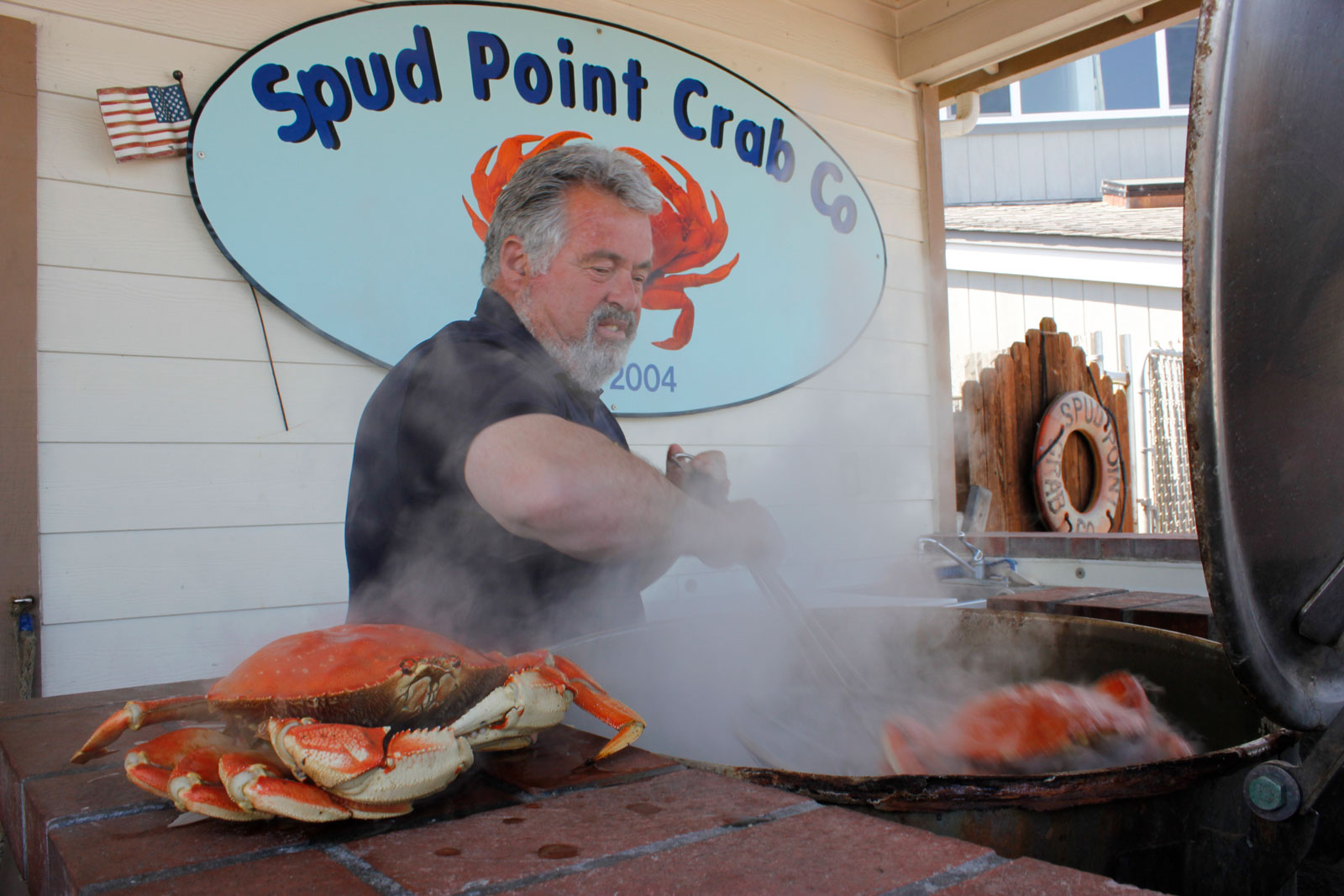 A man cooks crab on a BBQ in front of a blue sign 
