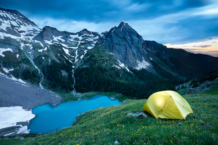 A yellow tent on a hill next to a mountain lake.