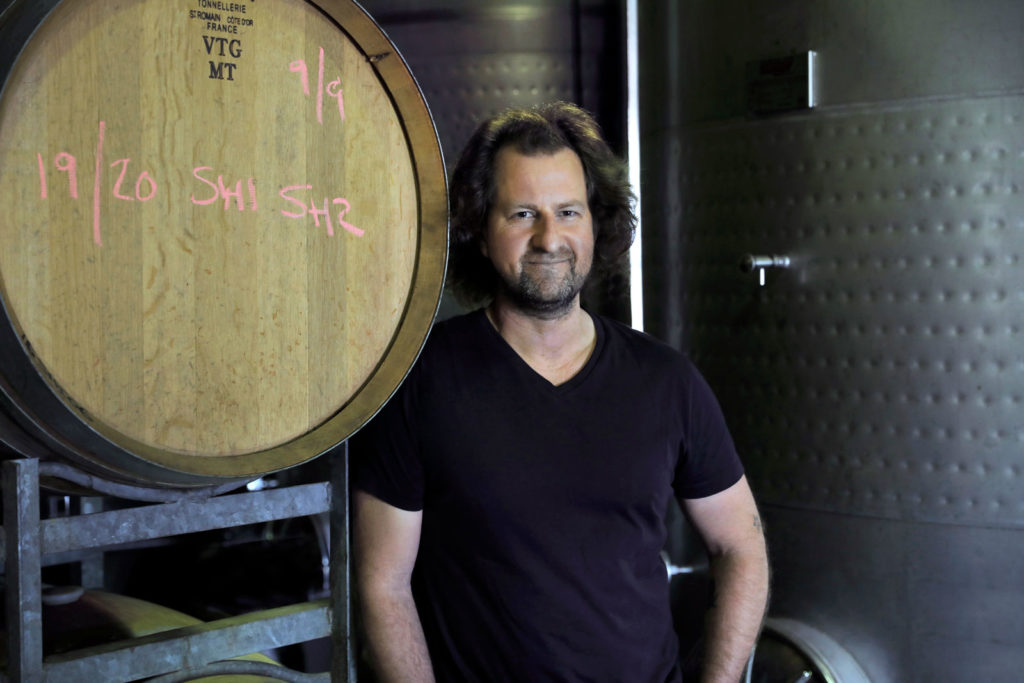 A smiling man standing next to a wine barrel.