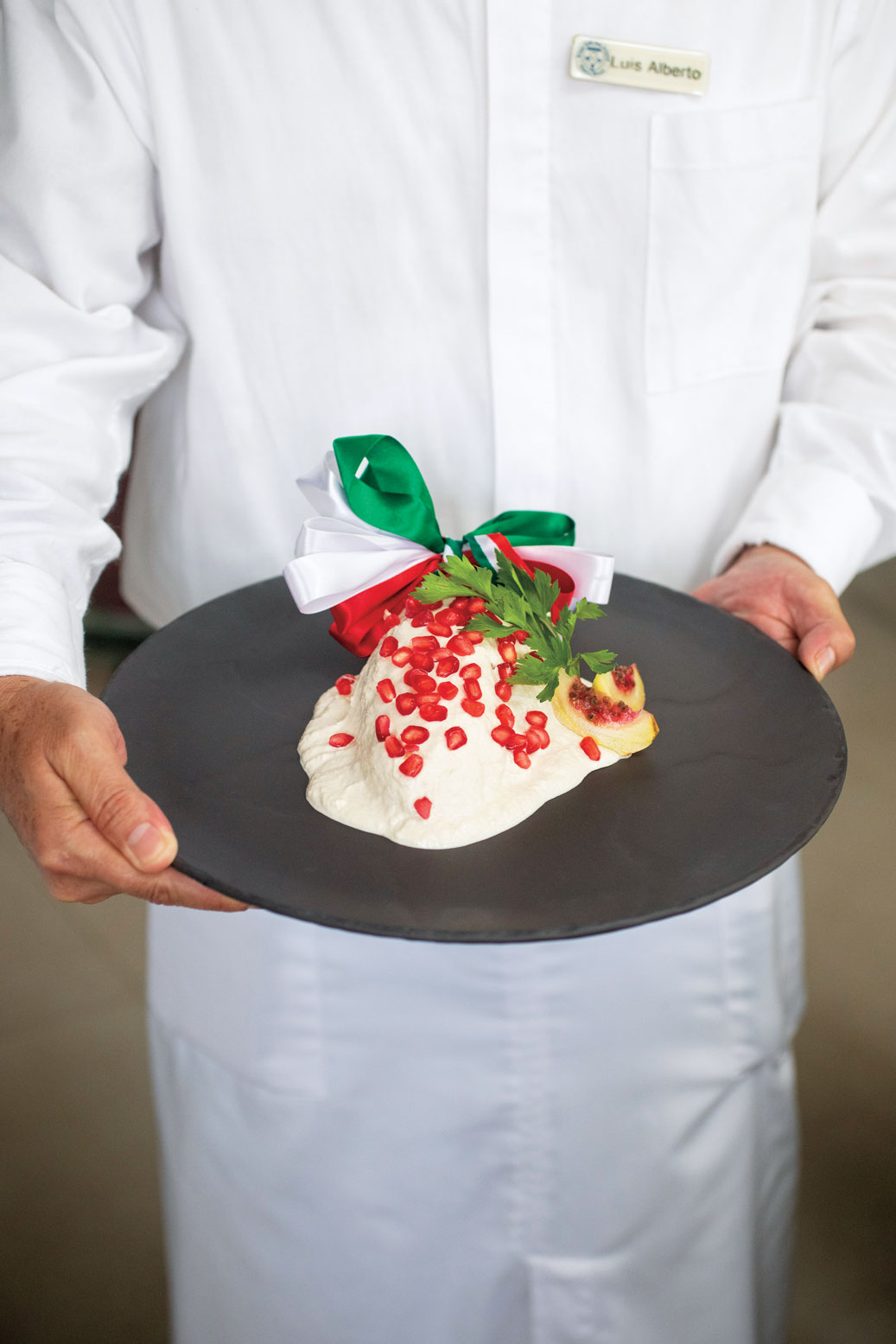 A server holding an ice dessert with fruits on a black plate.