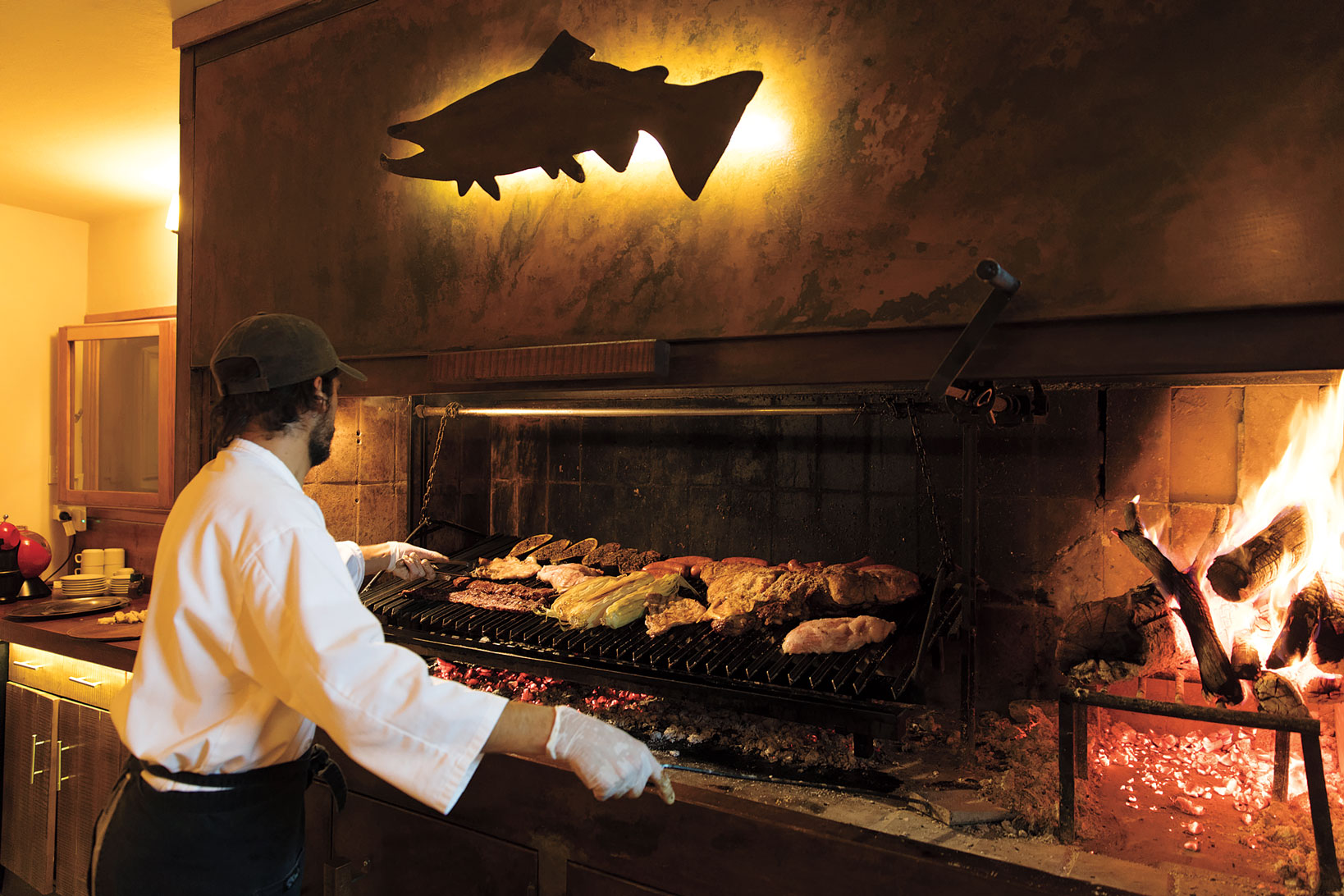 A men standing in front of a large grill laden with meat in a restaurant. 
