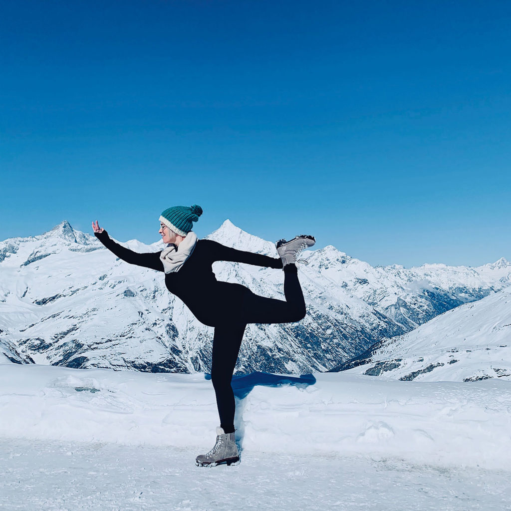 A woman doing a yoga posture in a snowy mountain landscape