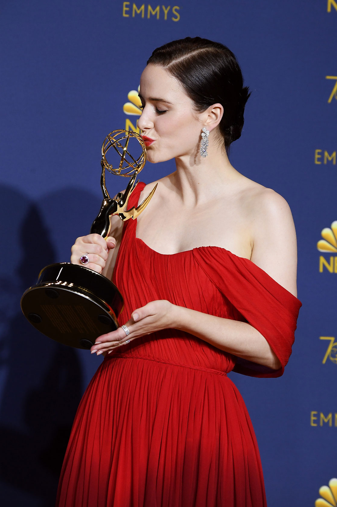 A woman wearing a red dress holding a golden trophy in her hands.