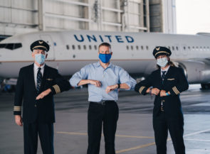 A pilot and two staff members standing in front of an airplane wearing masks.