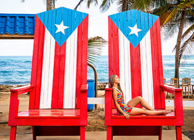 Woman lounges on two chairs painted with the Puerto Rican flag