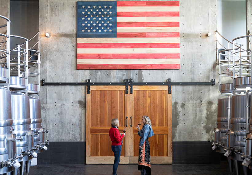 Two women standing under an American flag inside the winery of RdV Vineyards