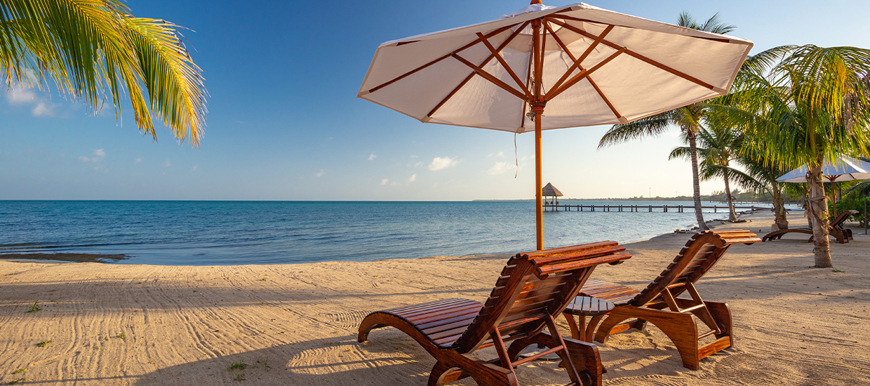 A pair of reclining beach chairs face the sunny horizon on the Sirenian Bay in Belize