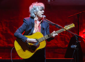 Singer Neil Finn playing an acoustic guitar at a post-lockdown concert in New Zealand