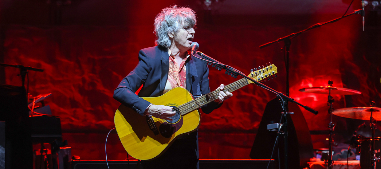 Singer Neil Finn playing an acoustic guitar at a post-lockdown concert in New Zealand